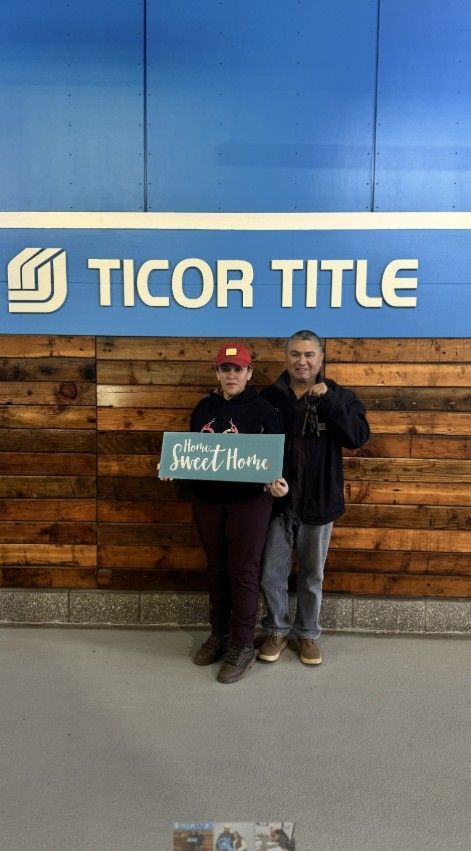 A man and a woman are standing in front of a ticor title sign.