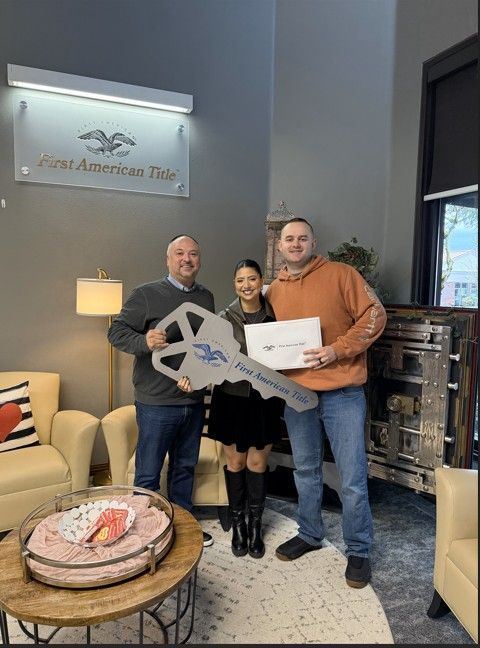 Two men and a woman are holding a large key in a living room.