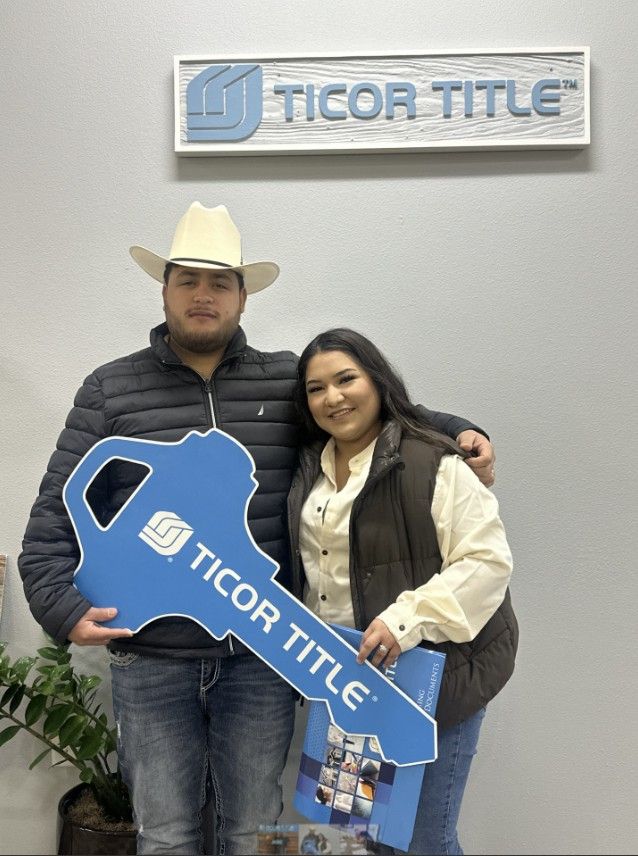 A man and a woman are holding a large blue ticor title key.