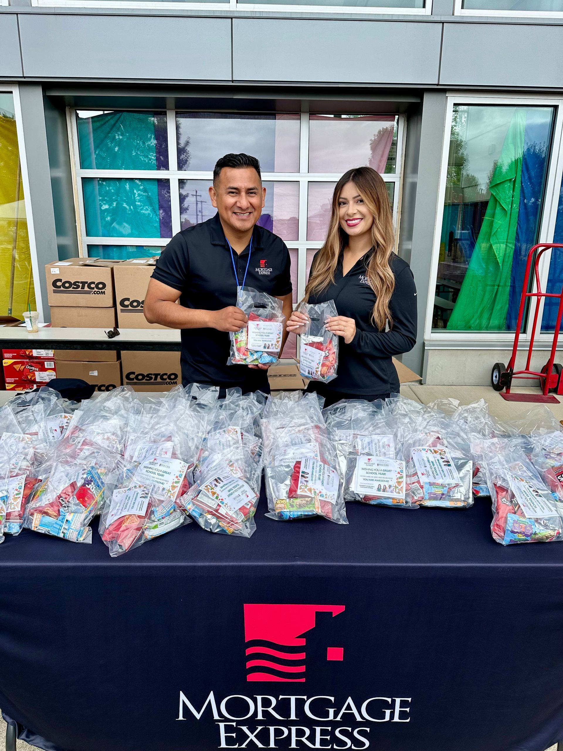 Two people from Mortgage Express holding bags of goodies at an outdoor event.