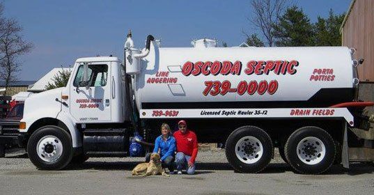 Man and woman and dog in front of Oscoda Septic truck