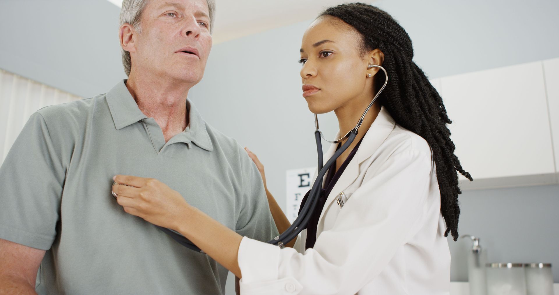 Doctor using stethoscope on patient in a hospital room, both smiling.