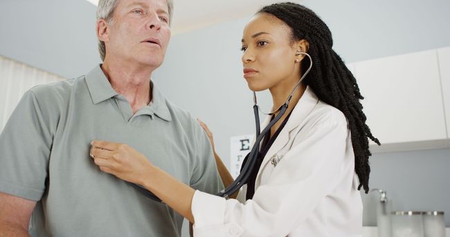 Doctor using stethoscope on patient in a hospital room, both smiling.