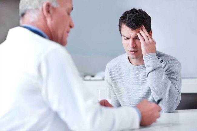Doctor and patient in consultation. Man with hand on forehead, looking distressed, while doctor writes.