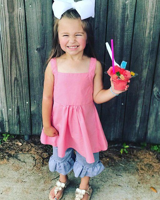 A little girl in a pink dress is holding a cup of ice cream.