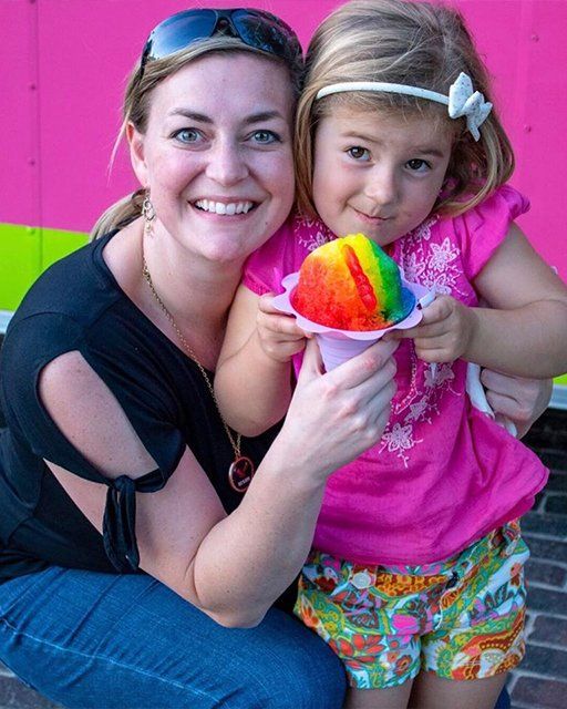A woman and a little girl are holding a rainbow colored ice cream cone