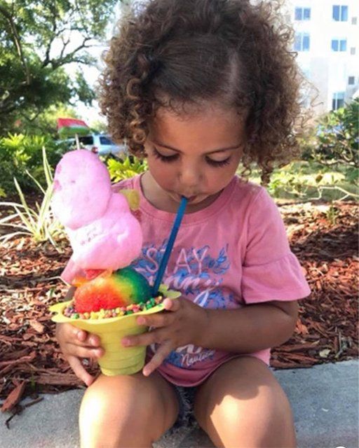 A little girl in a pink shirt is drinking from a cup of ice cream