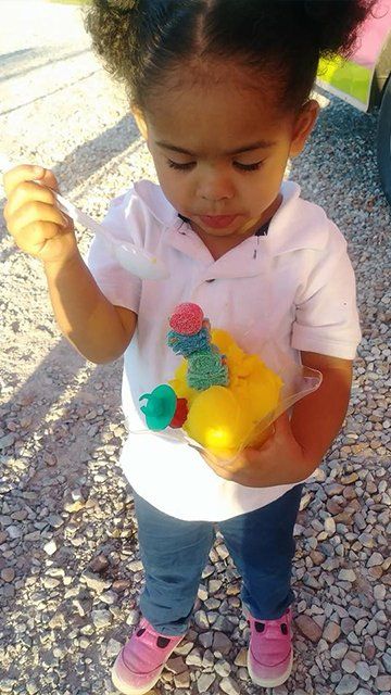 A little girl is standing on a gravel road holding a bag of gummy bears.