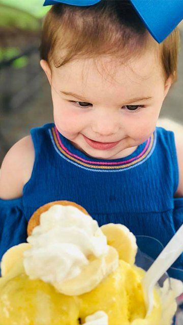 A little girl is eating a bowl of ice cream with bananas and whipped cream.