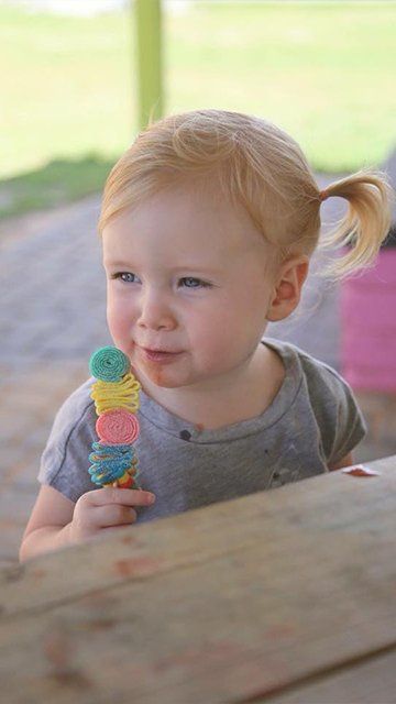 A little girl is eating an ice cream cone at a picnic table.