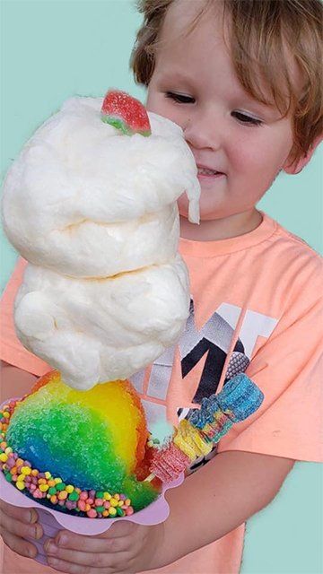 A young boy is holding a cup of cotton candy with a watermelon on top.
