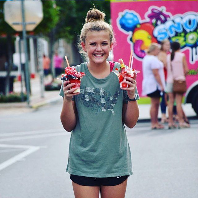 A girl is holding two cups of ice cream in front of a pink truck that says ' swirl ' on it