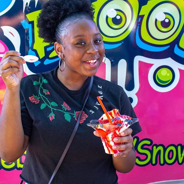 A woman holding a cup of ice cream in front of a sign that says snow