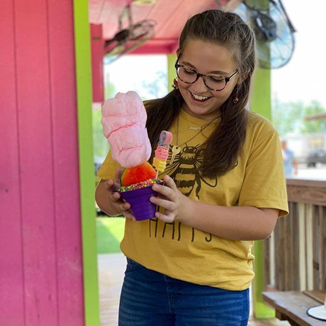 A girl in a yellow shirt is holding a cup of ice cream
