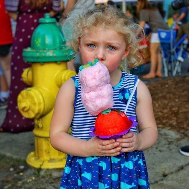 A little girl is eating cotton candy in front of a fire hydrant