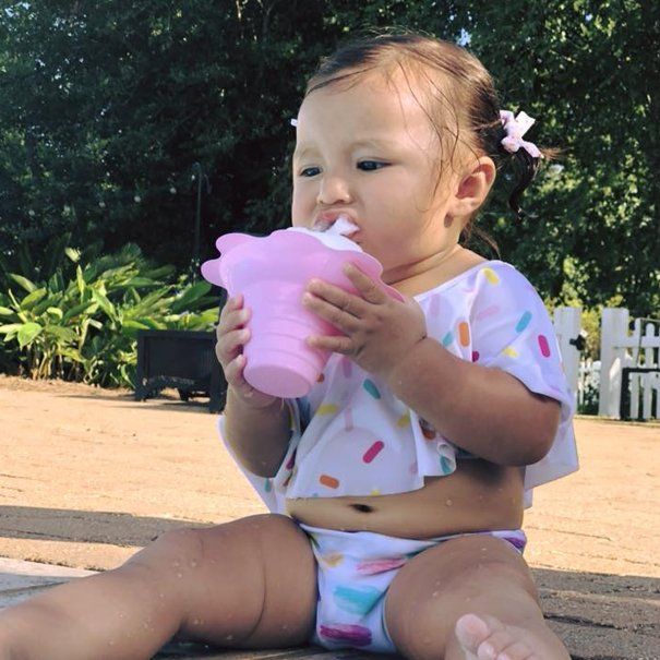 A baby girl is sitting on the ground drinking from a pink cup
