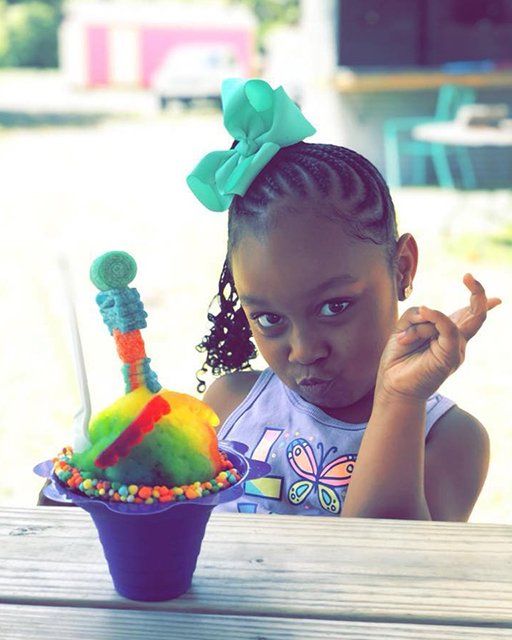 A little girl sitting at a table with a cup of ice cream