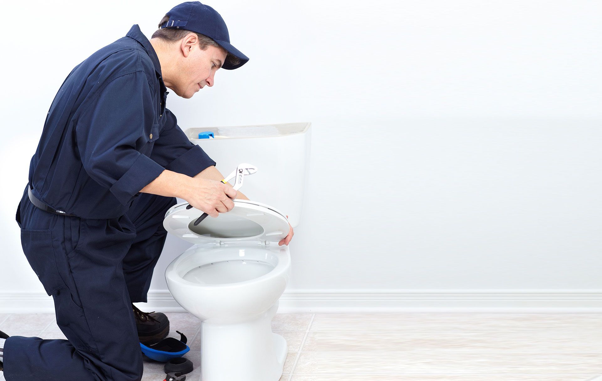A technician in a navy blue uniform kneels to install a white toilet seat.