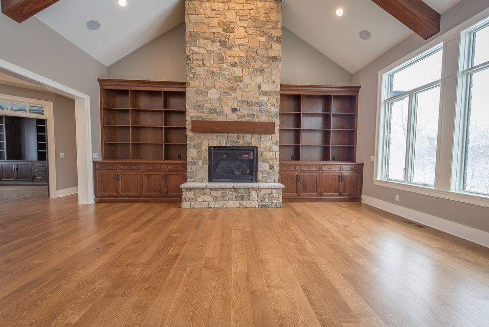 An empty living room with hardwood floors and a stone fireplace.