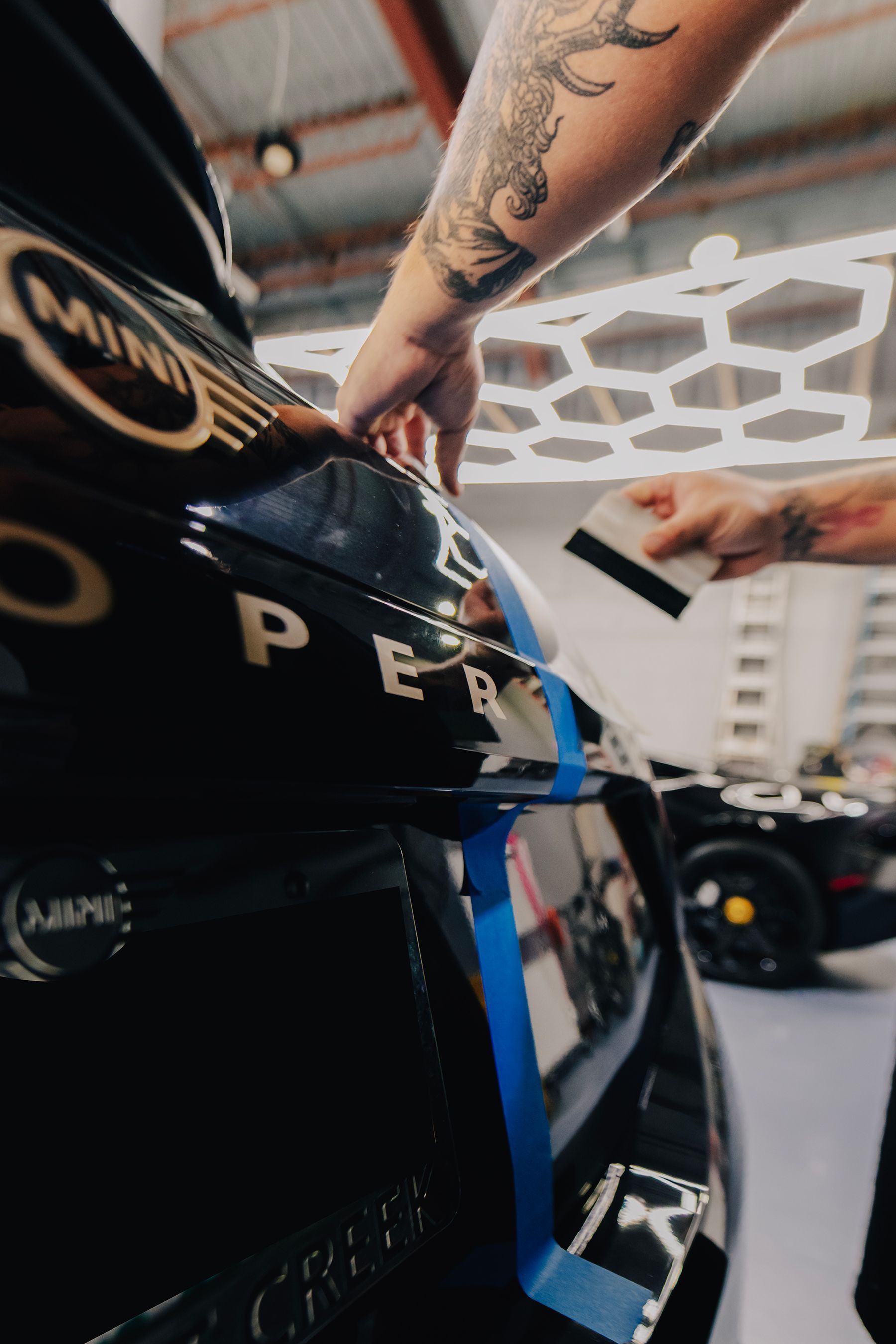Person applying black vinyl to the roof of a blue car. Garage setting.