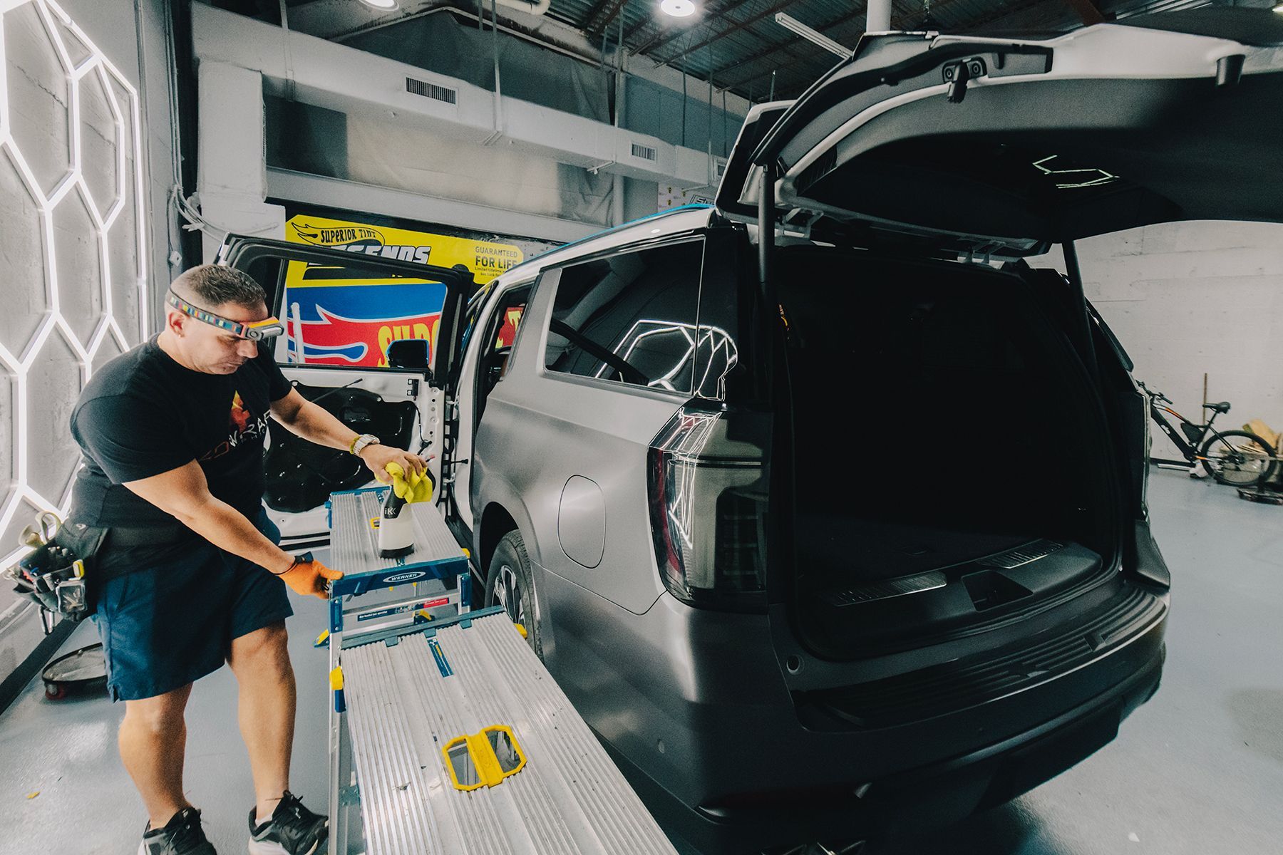 A person working on a car in a workshop. Car's rear door is open. The person is wearing safety glasses.