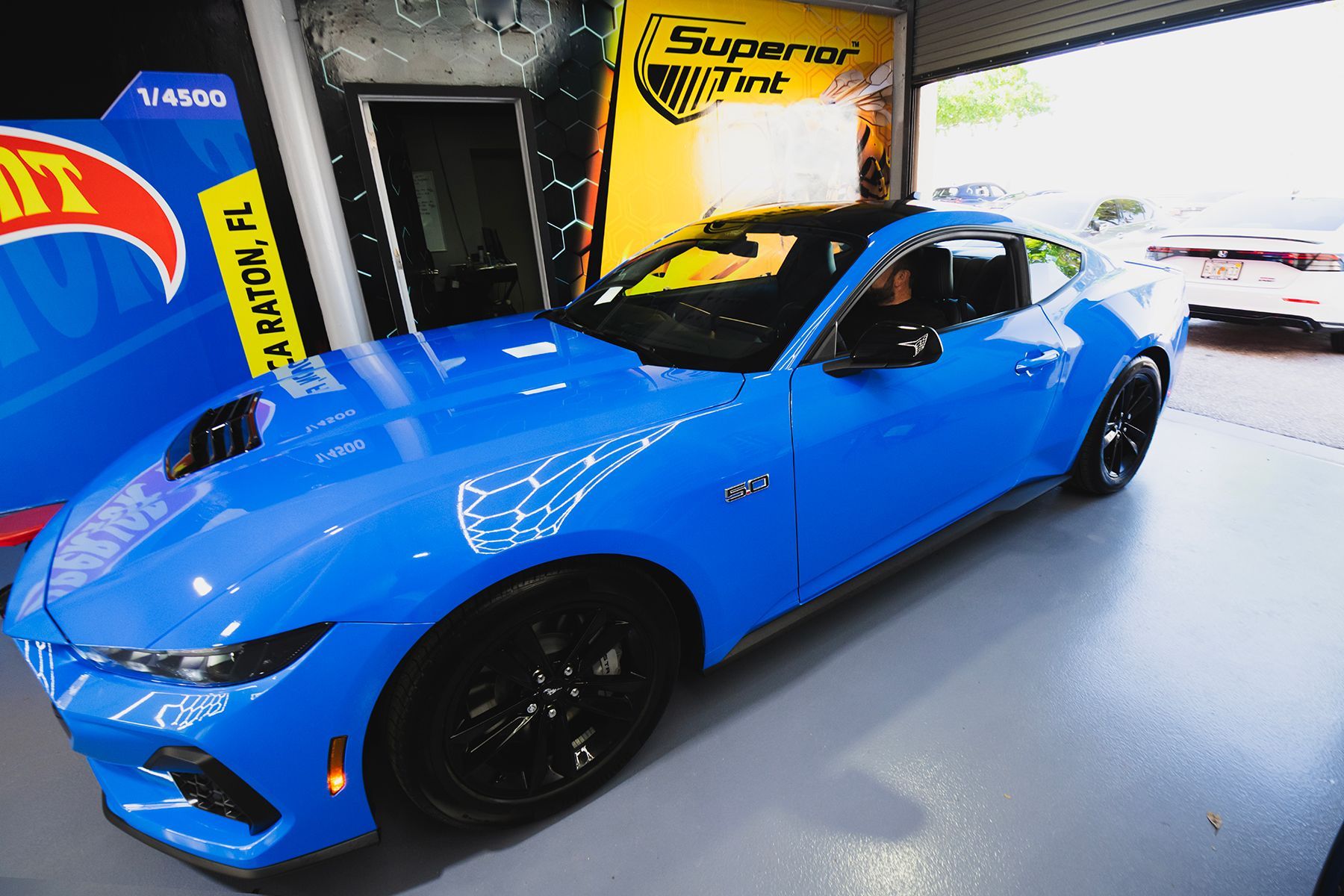 Bright blue sports car with black wheels parked inside a garage, possibly for tinting.