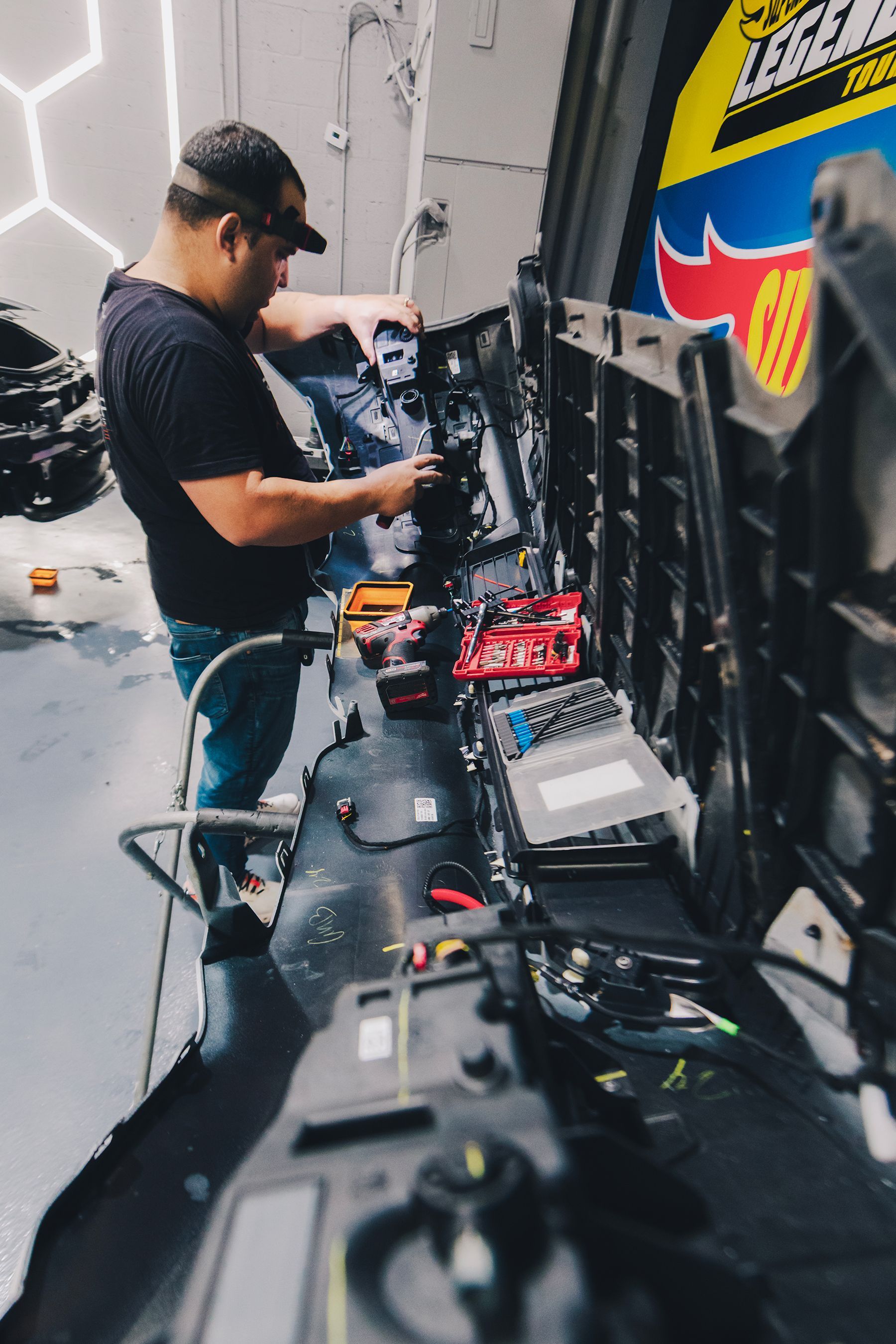 Man in a cap working on electronic components, a row of equipment visible, indoors.