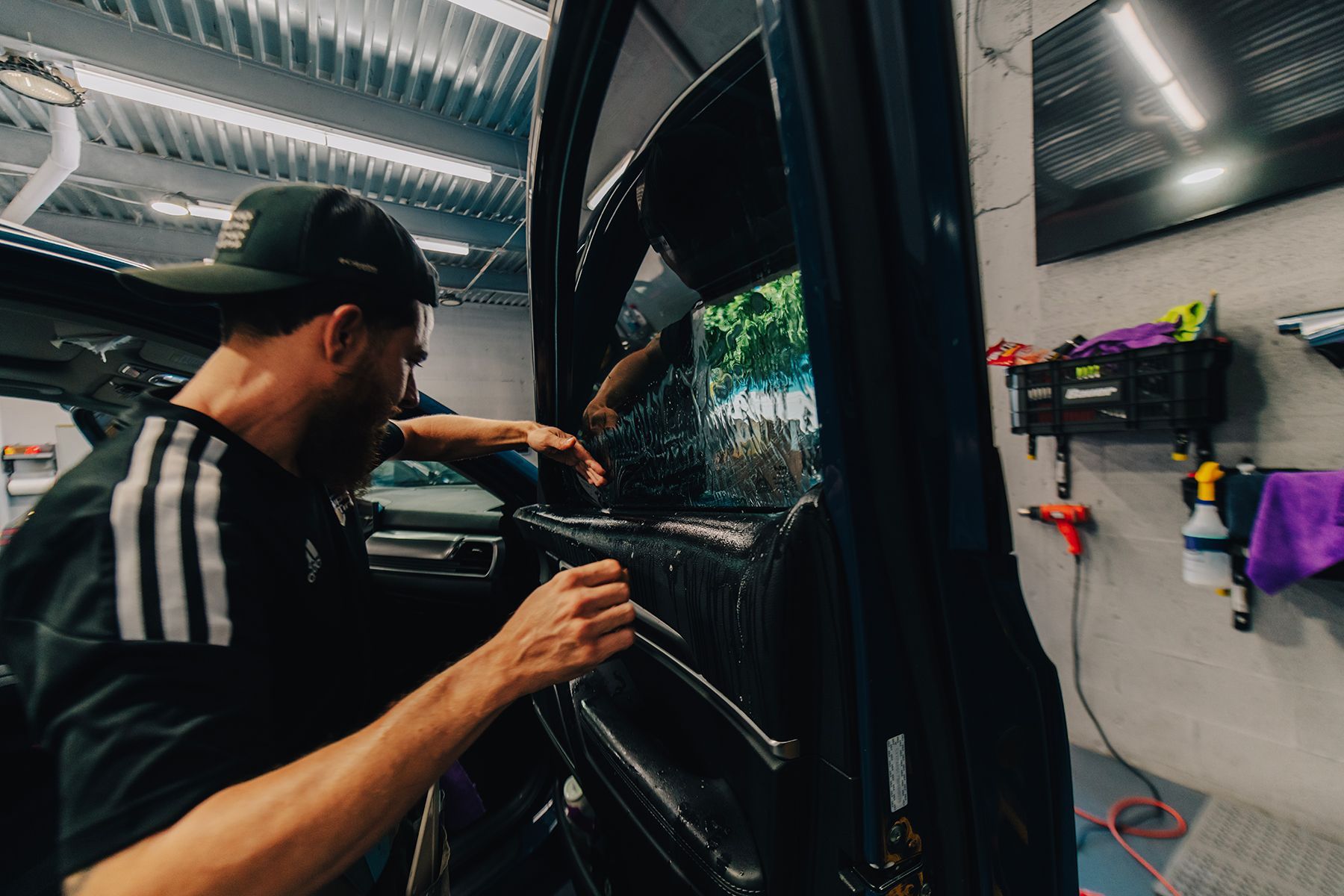 Person applying tint to a car window inside a shop.