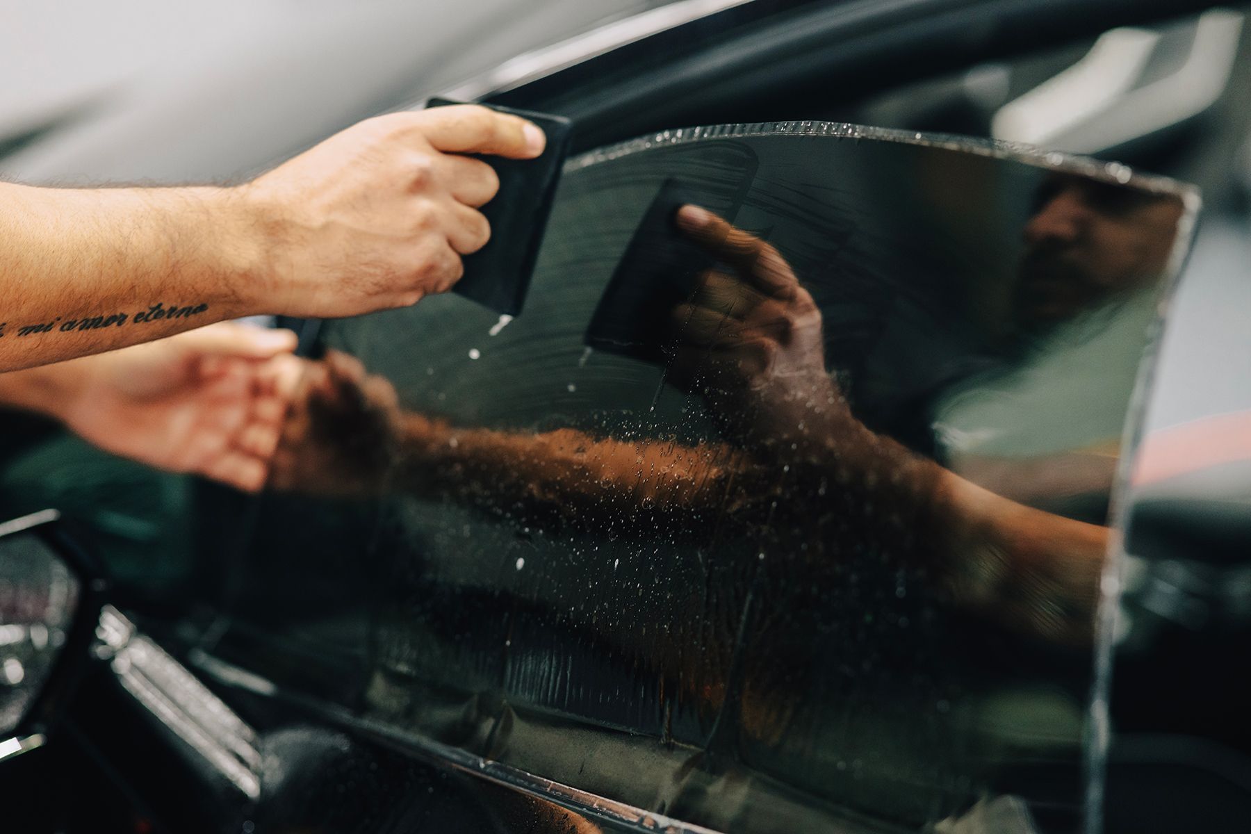 Person applying tint to a car window with a squeegee.