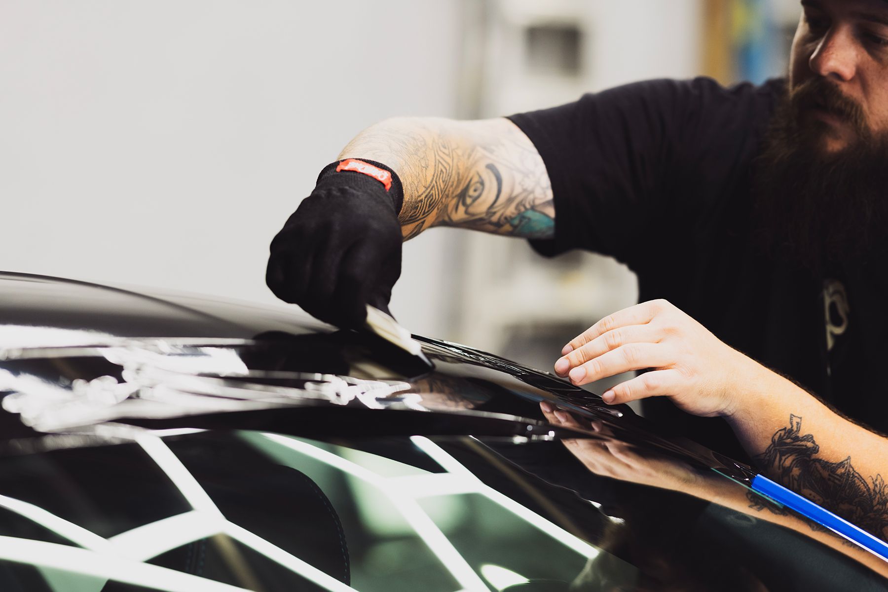 Person in black gloves installing film on a car roof, indoors.