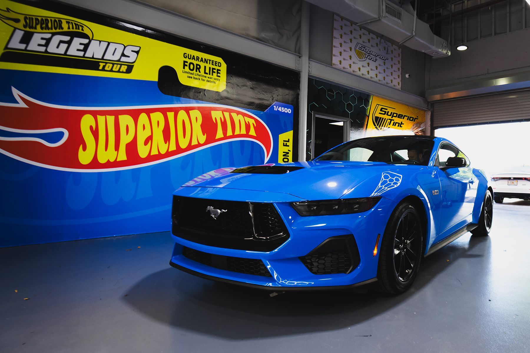 Blue Ford Mustang in a garage with a Hot Wheels backdrop.
