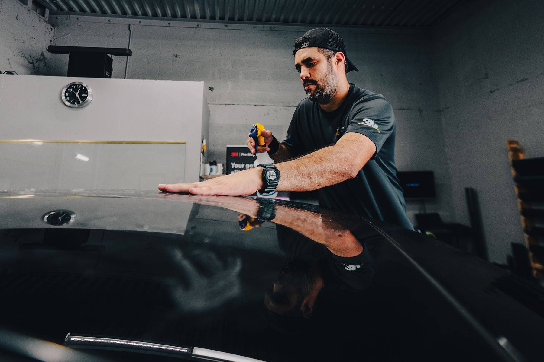 Man applying film to a car roof in a garage, using a tool.