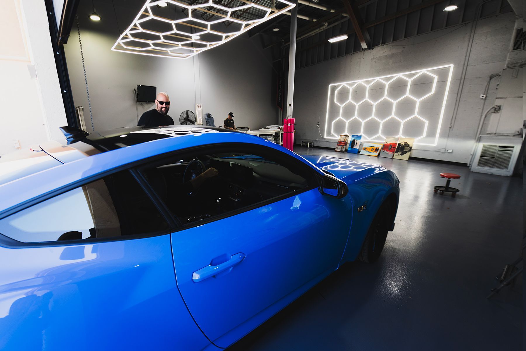 Blue sports car in a garage with honeycomb-shaped lights on the ceiling and wall.