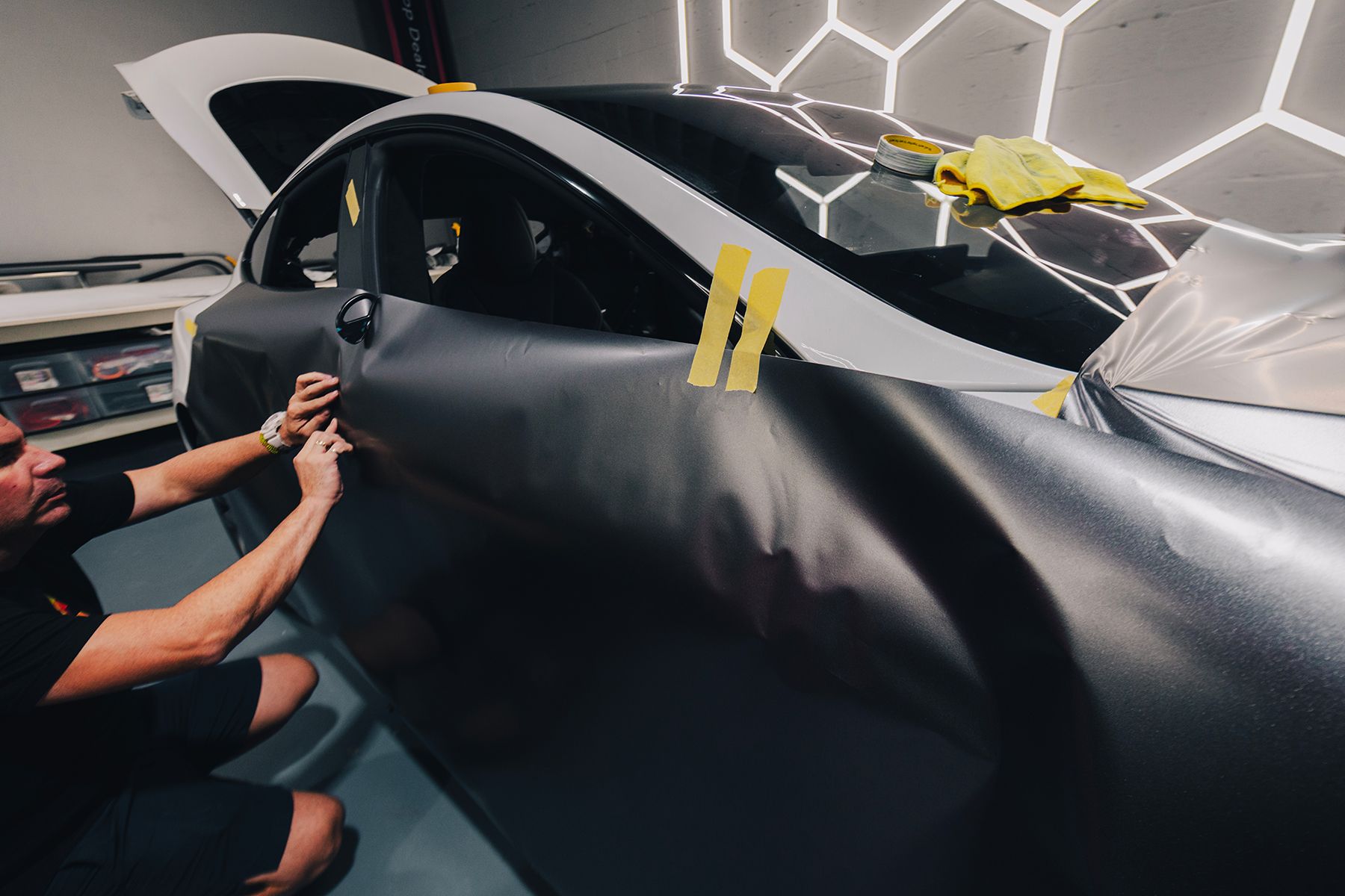 Person applying carbon fiber vinyl wrap to a car door in a garage.