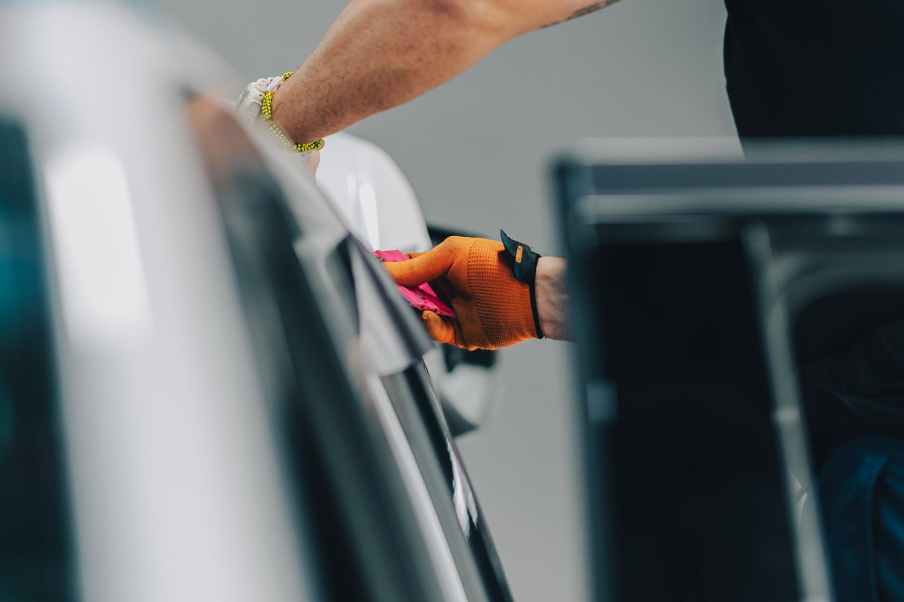 Person wearing gloves cleaning a car door with a pink cloth.