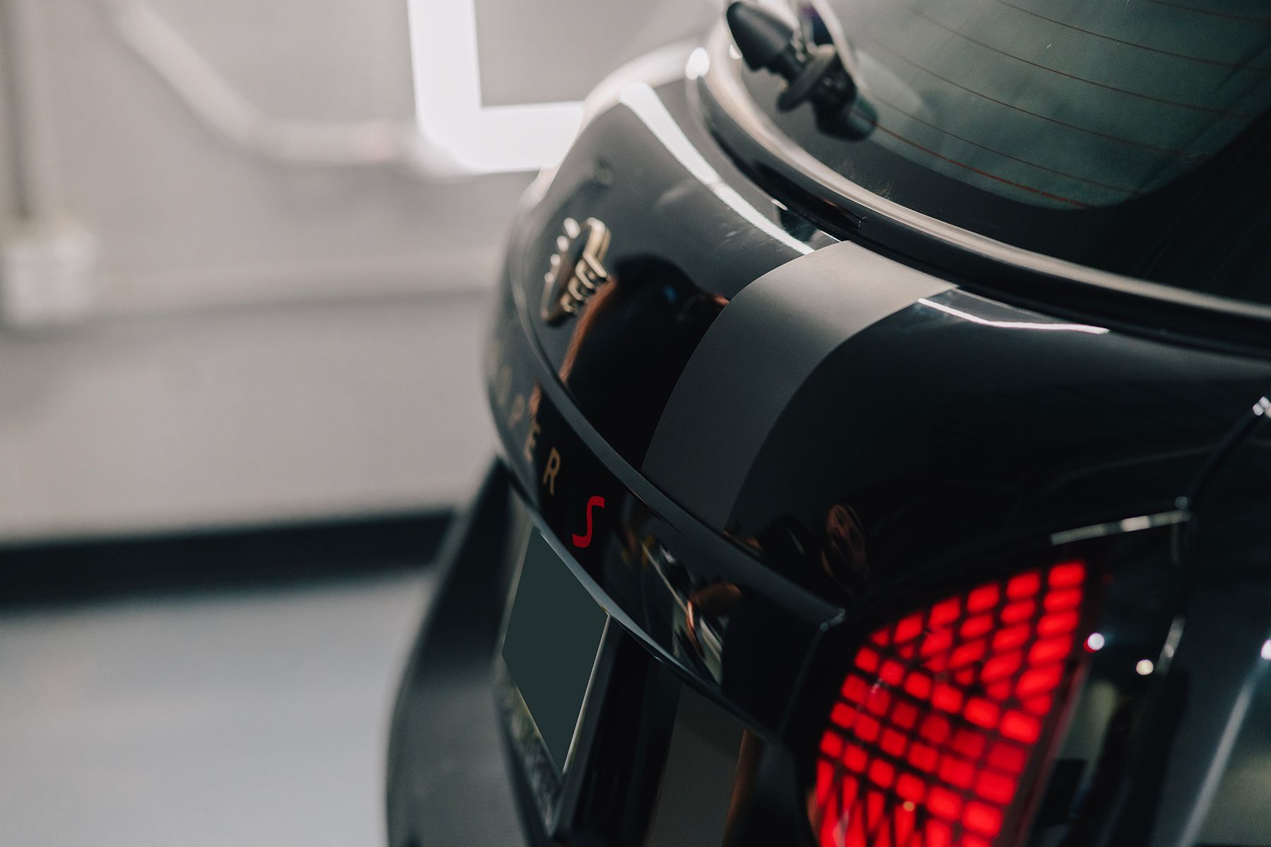 Black car's rear, with a red taillight and a partial view of a grey stripe, indoors.