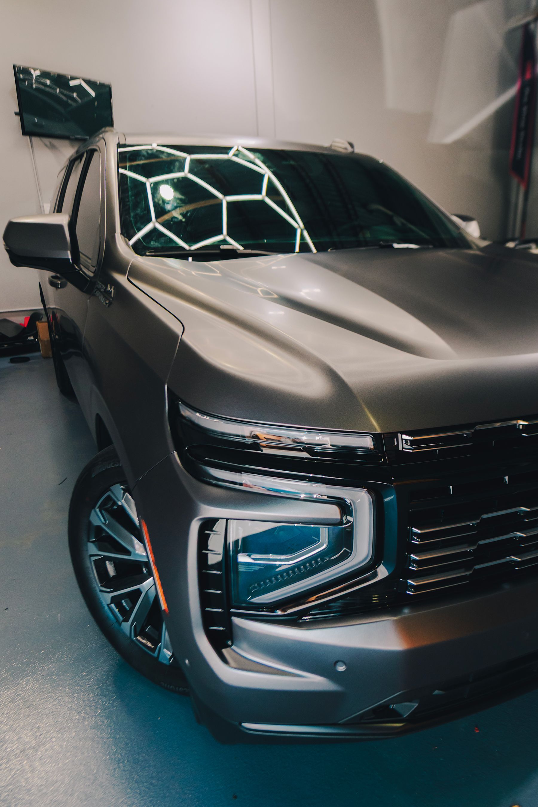 Gray SUV parked in a garage with geometric lighting reflected in the windshield.