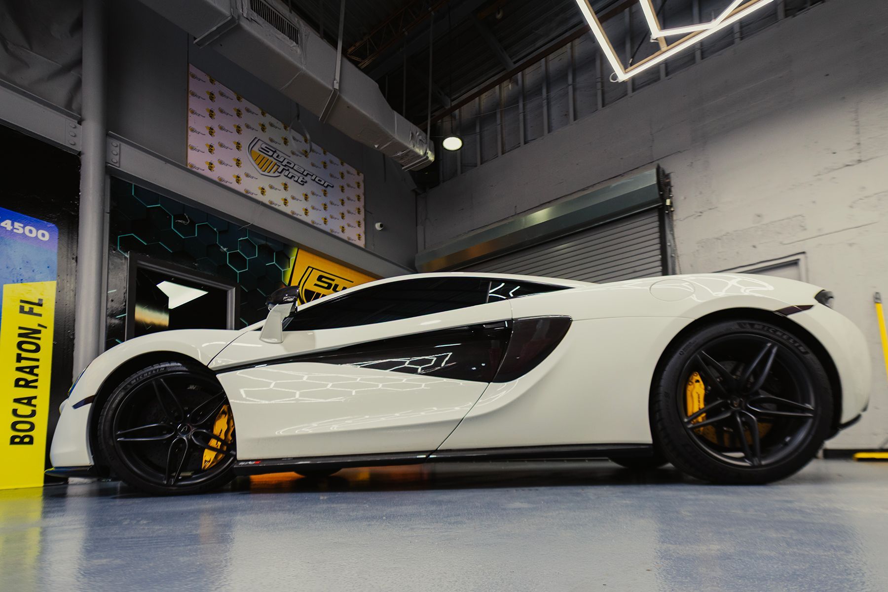 White McLaren sports car with black accents and yellow brake calipers in a garage.