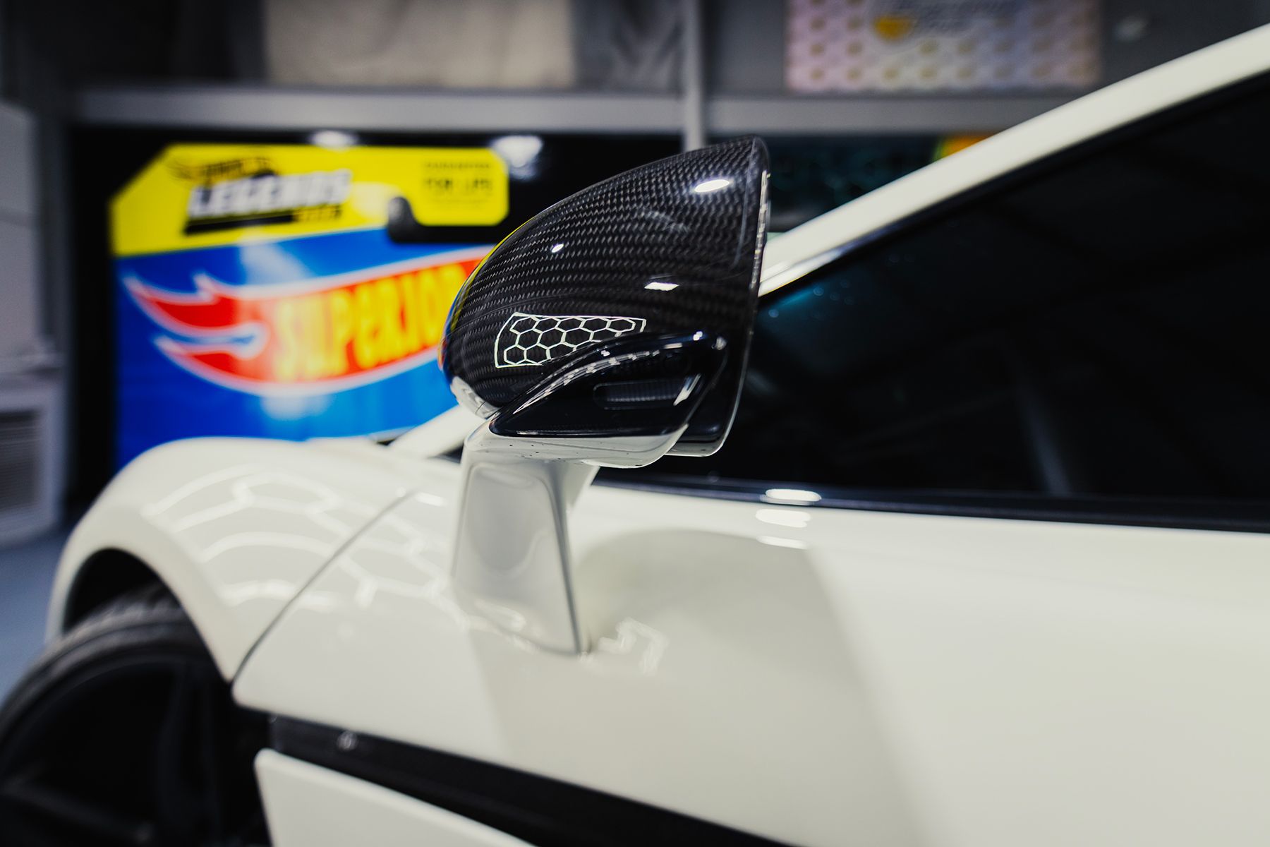 White car with a carbon fiber side mirror, parked indoors.