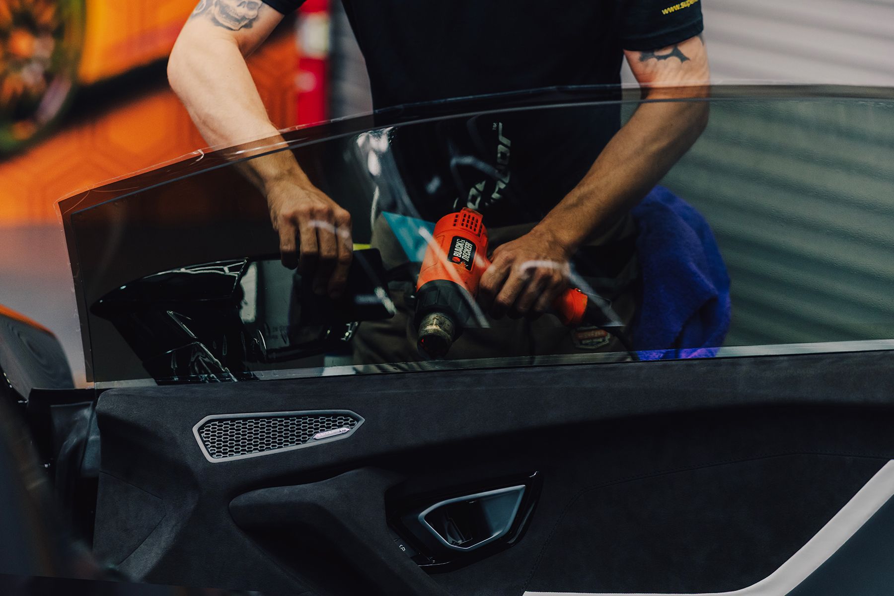 Person uses a heat gun on car window, applying tint. Inside of a vehicle.