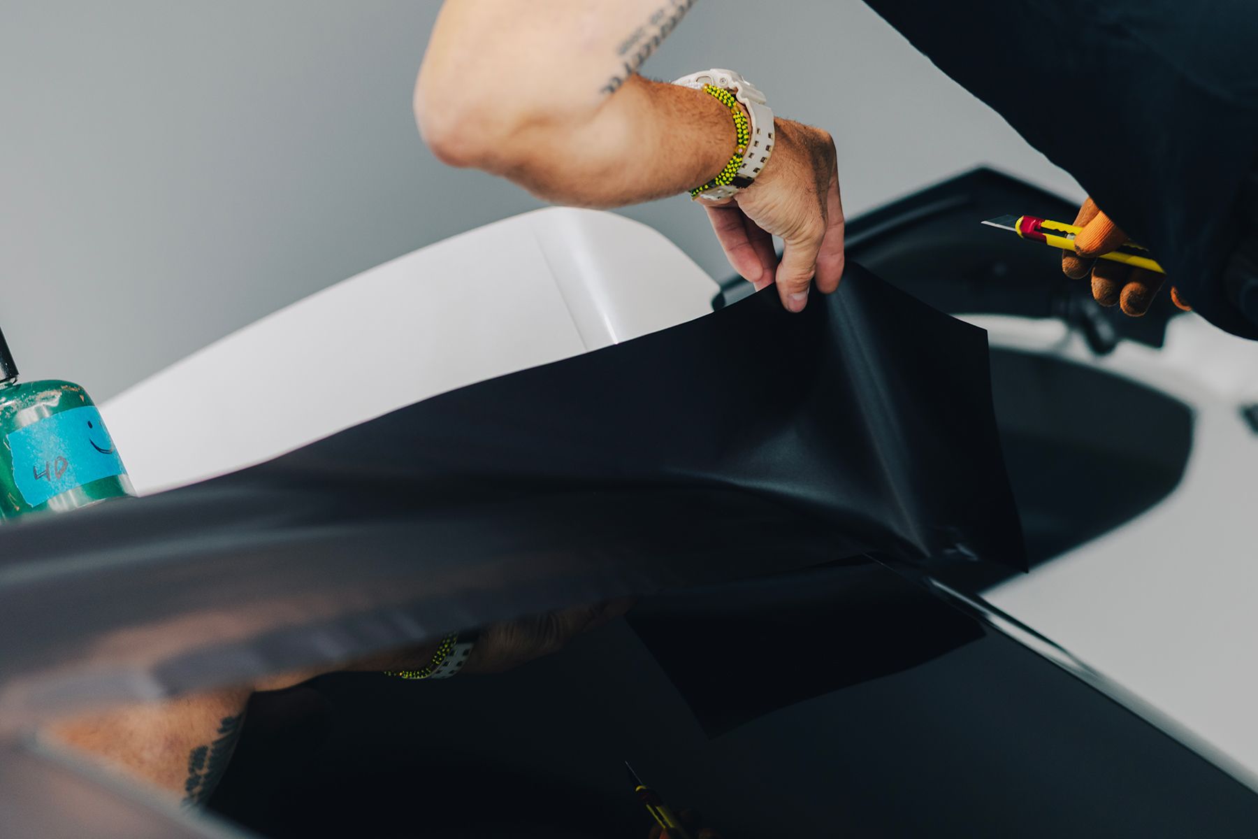 Person applying a dark film to a car's surface with a tool.