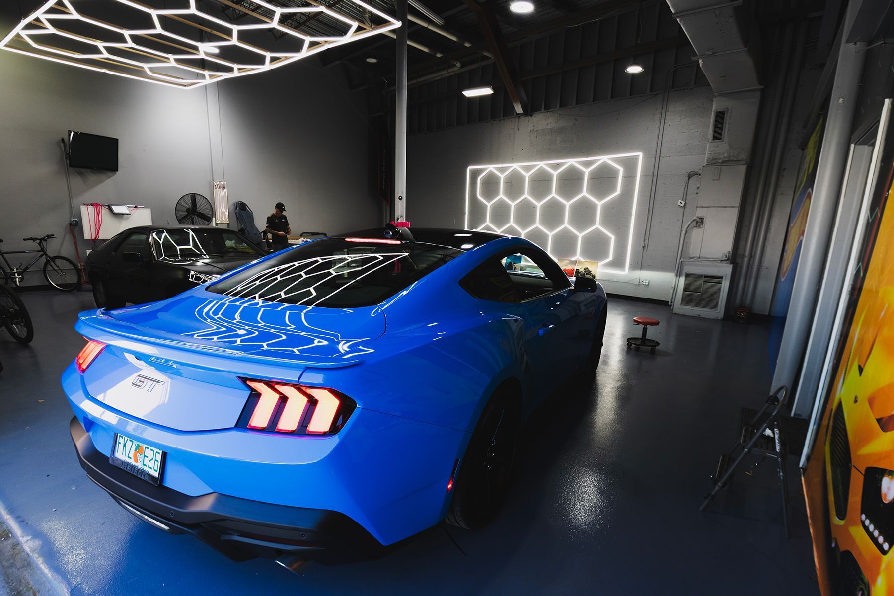 Blue Ford Mustang inside a garage with honeycomb-shaped lights on the ceiling and wall.