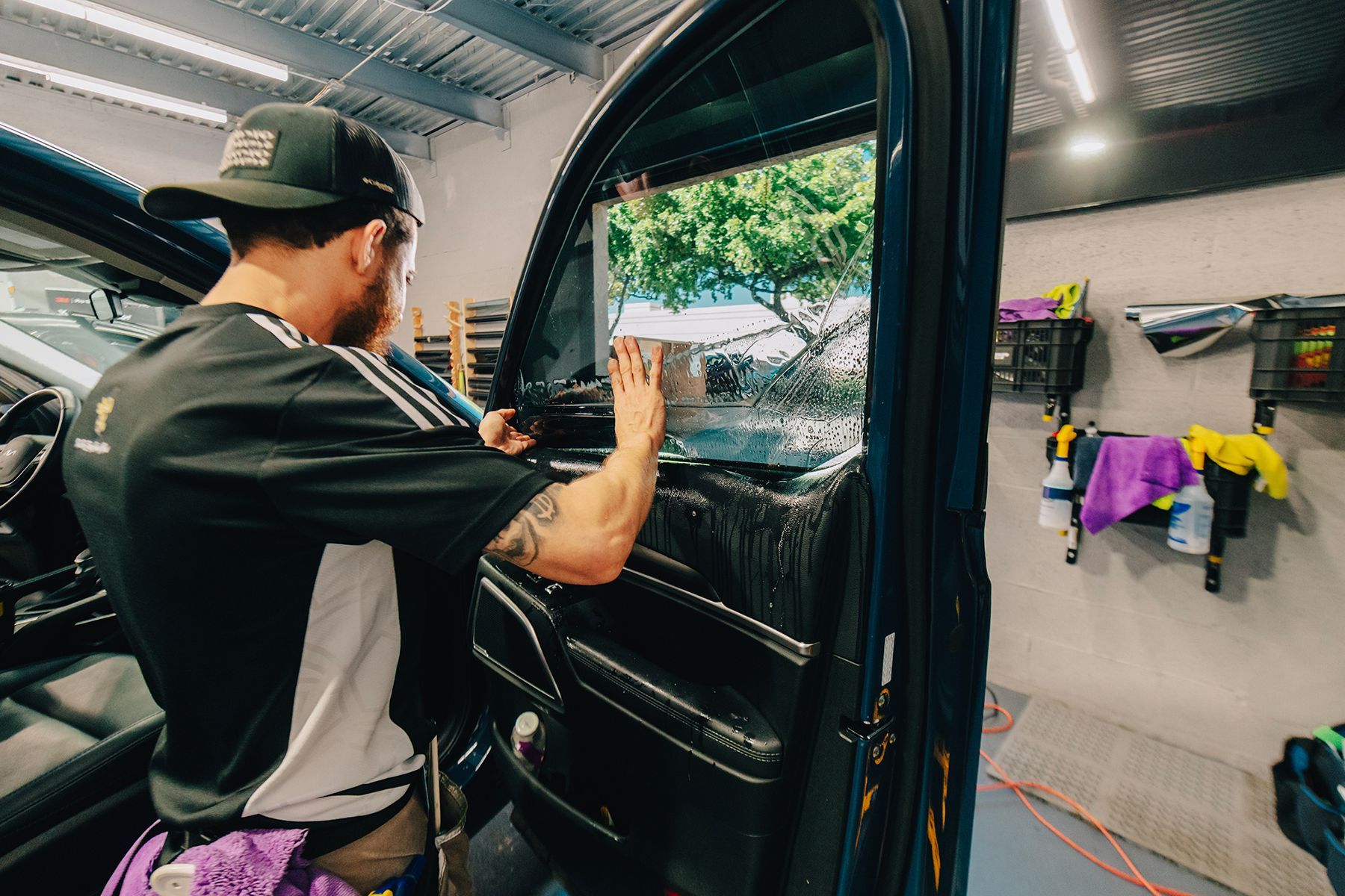 Person applying tint to a car window inside a workshop.