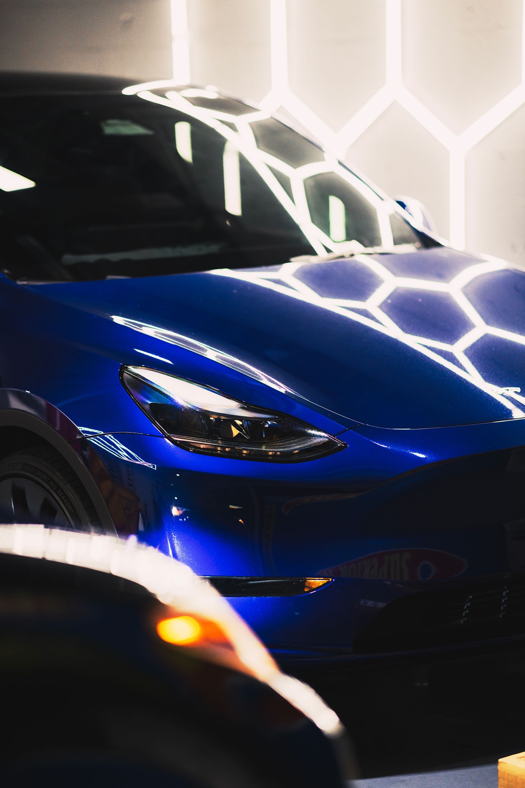 Blue Tesla car under bright hexagonal lights.