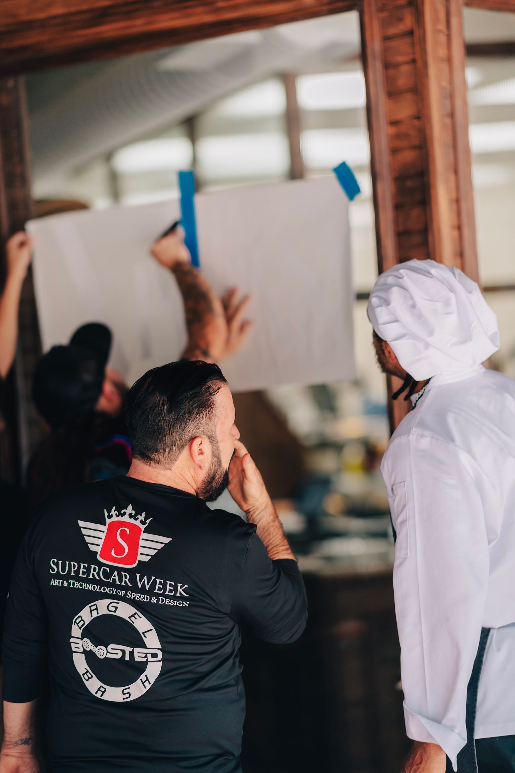 People hanging a white paper on a glass door. Chef looks on.