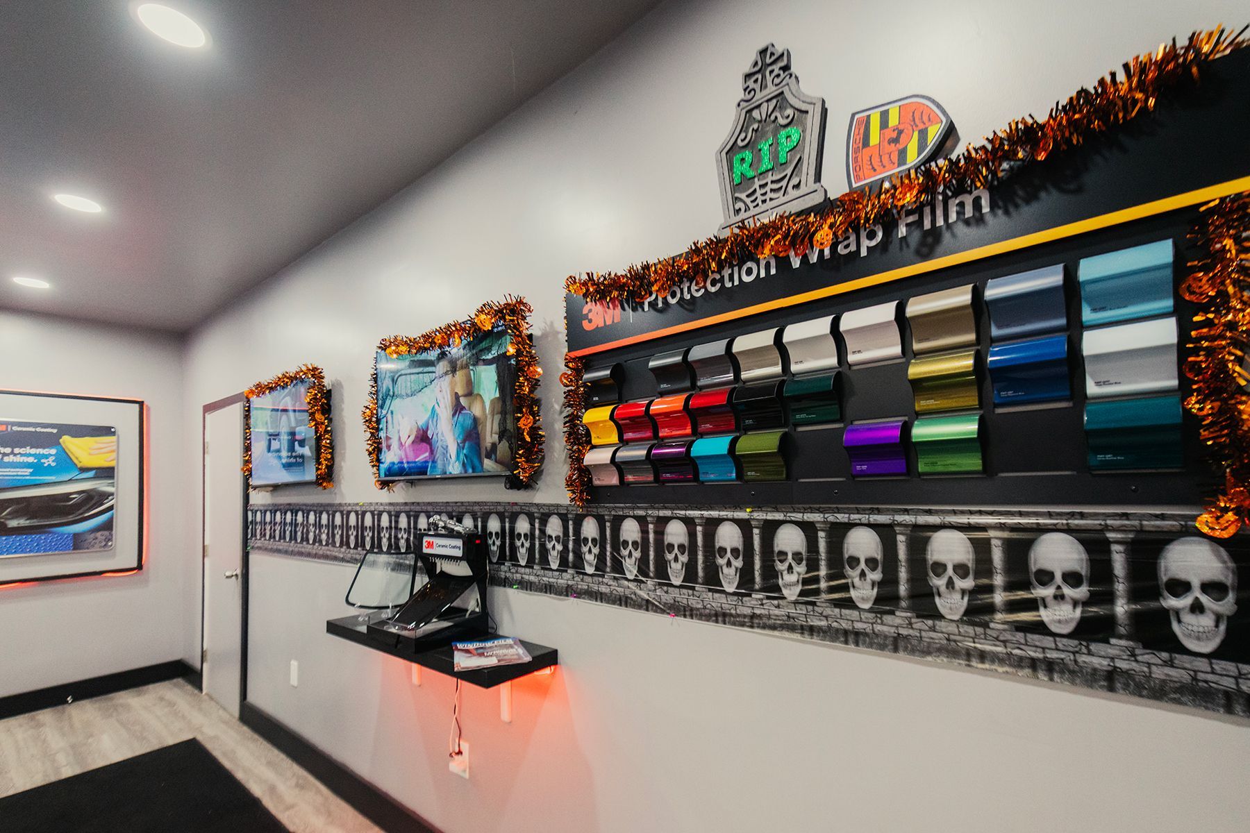 A display of car wrap film color swatches in a shop, decorated with Halloween garlands and skull images.