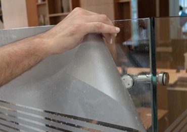 Hand peeling a frosted film from a glass panel on a door.