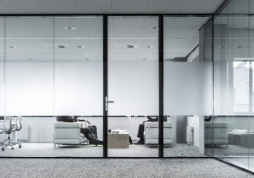 Modern office space with glass walls. Two people in chairs, one using a laptop, in a room with frosted privacy glass.