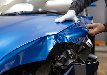 Hands installing blue vinyl wrap on car hood.