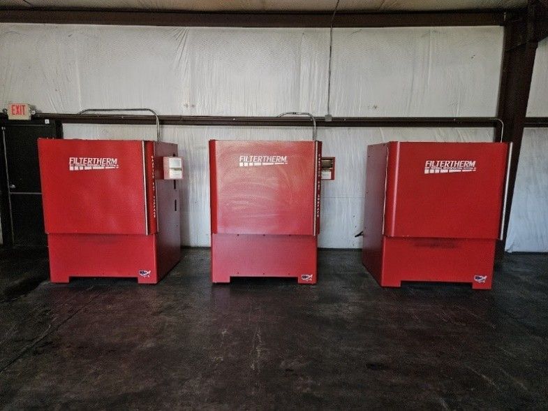 Three red high-capacity ovens lined up against a warehouse wall on a concrete floor.